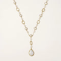 Y-shaped gold necklace with alternating geometric links, freshwater pearls, and baroque pearl pendant on cream background