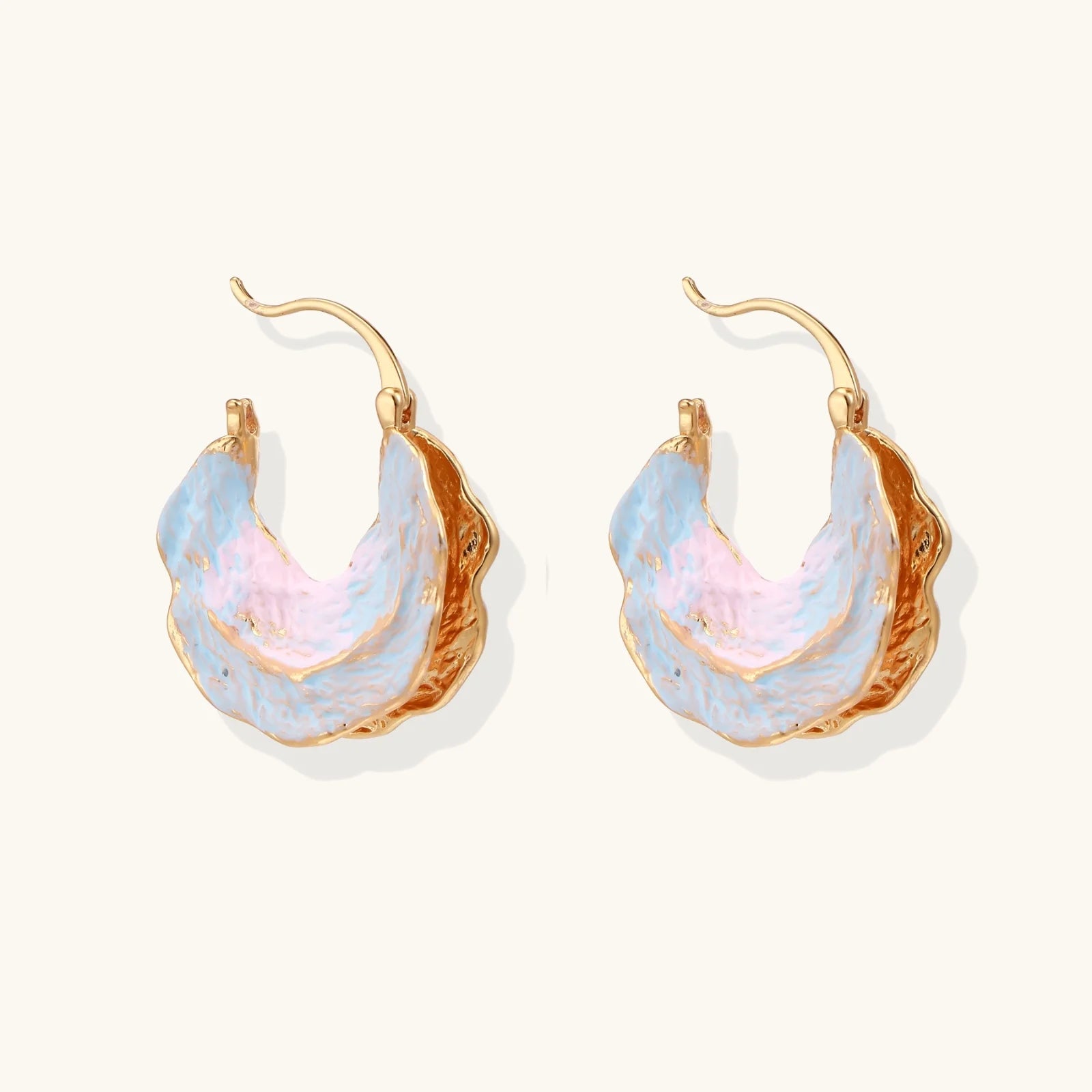 Shell-shaped hoop earrings with iridescent blue-pink enamel and gold trim on cream background