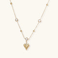 Delicate gold-plated necklace with bezel-set crystals and small heart pendant on beige background