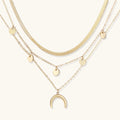 Four-layer gold necklace with herringbone chain, disc charms, and crescent moon pendant on cream background