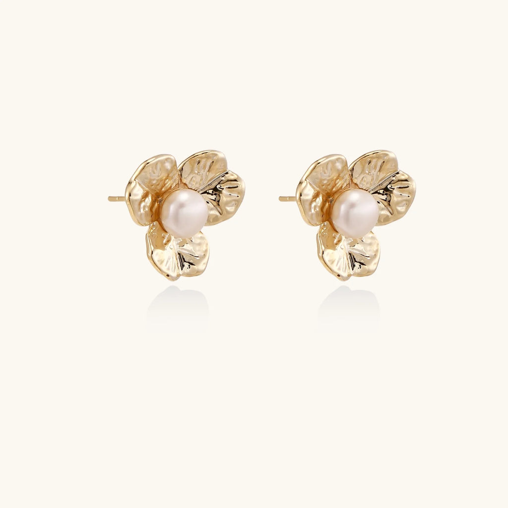 Gold-plated flower stud earrings with textured petals and centered freshwater pearl on beige background