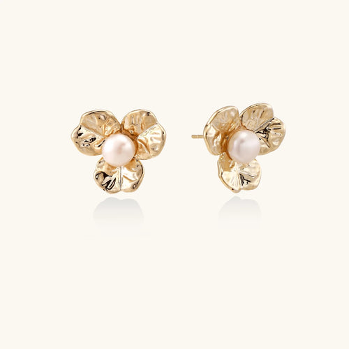 Gold-plated flower stud earrings with textured petals and centered freshwater pearl on beige background
