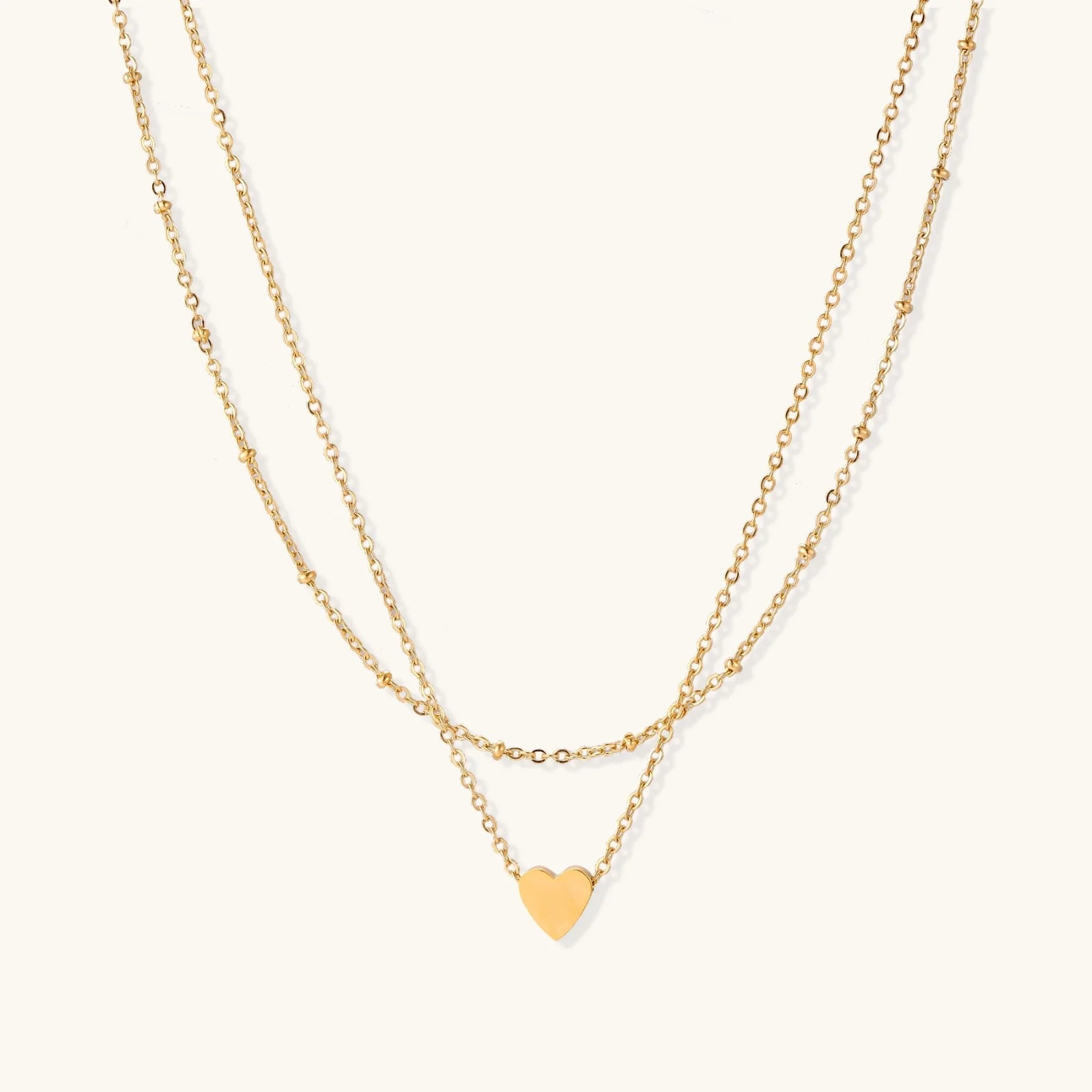 Delicate double-chain gold necklace with tiny heart pendant on cream background