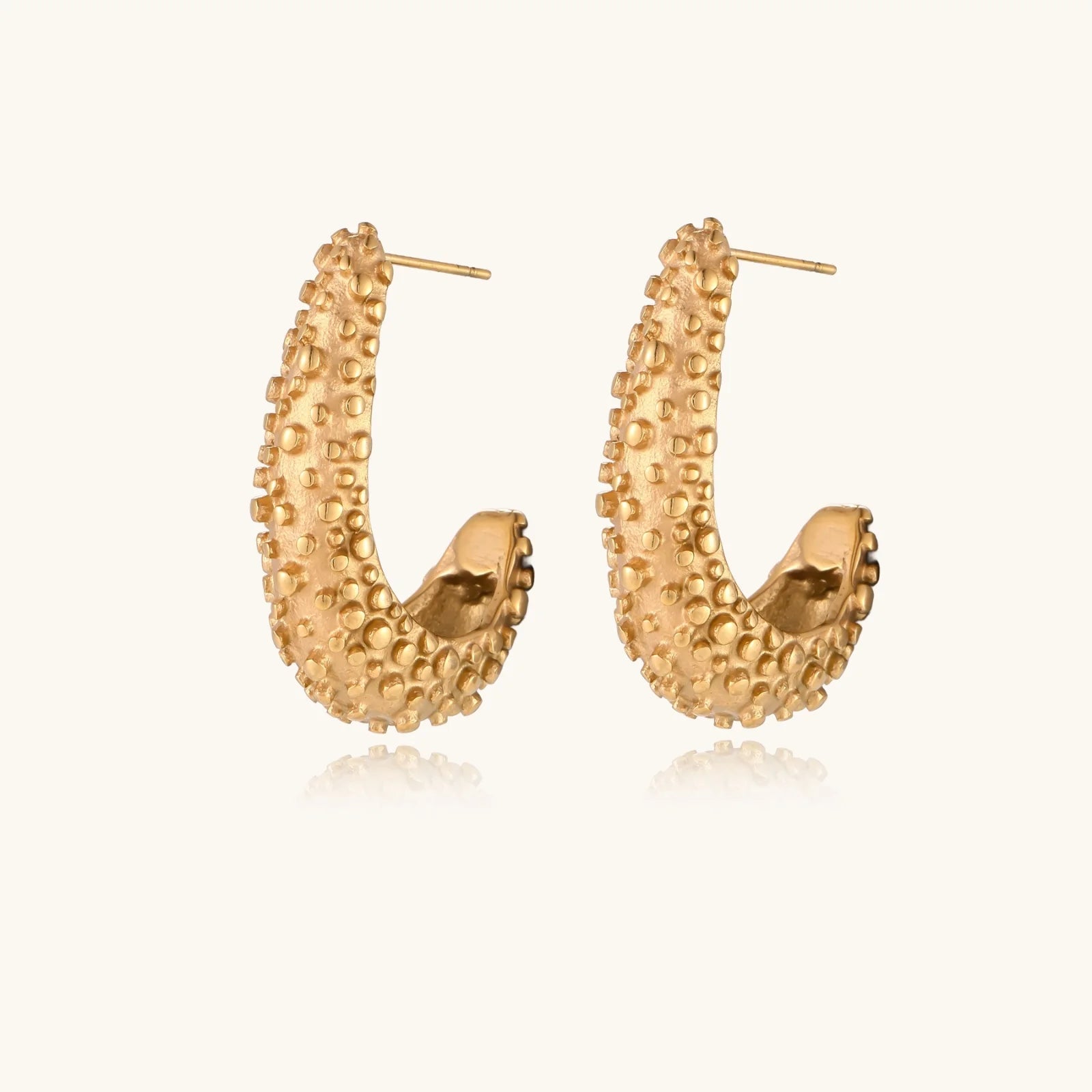 Curved gold hoop earrings with raised granulated texture resembling sea urchin surface on cream background